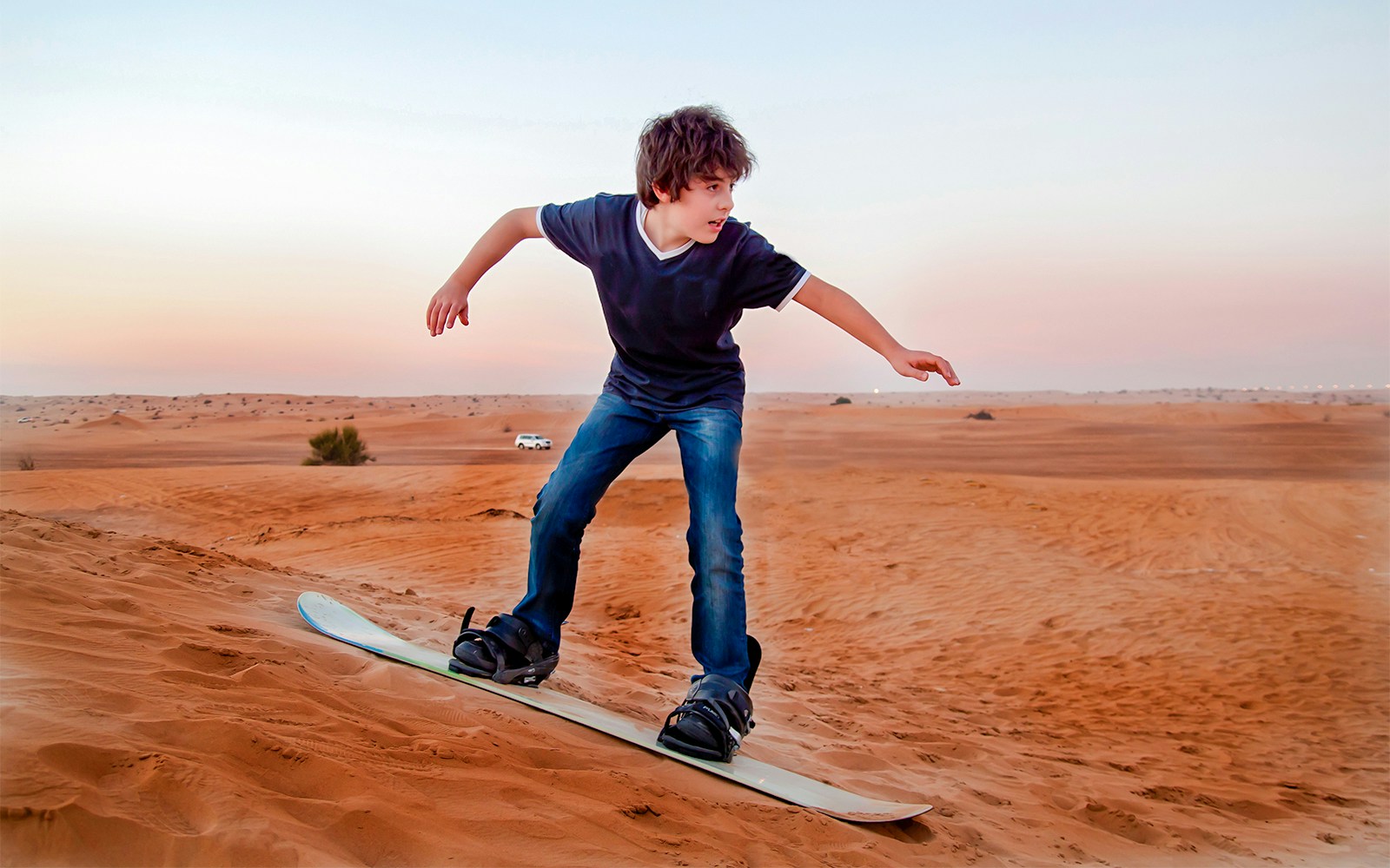 Child sandboarding on a dune in Dubai desert.