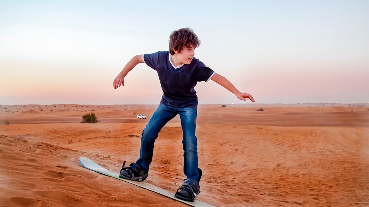 Enfant faisant du sandboarding dans le désert de Dubaï