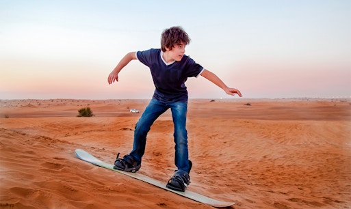 Child sandboarding on a dune in Dubai desert.