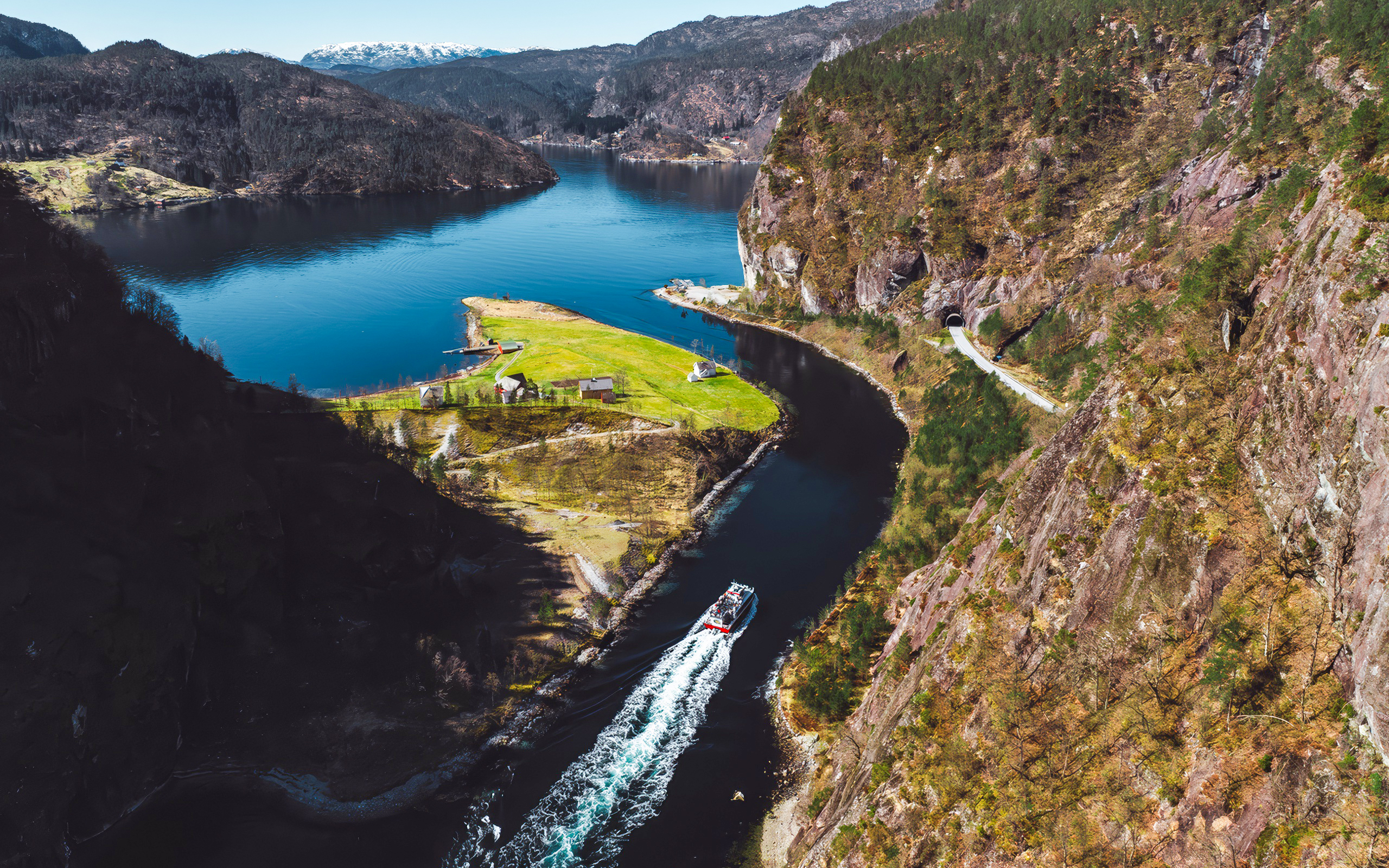 Cruise boat navigating Mostraumen Fjord near Bergen, surrounded by steep cliffs and lush landscape.