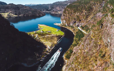 Cruise boat navigating Mostraumen Fjord near Bergen, surrounded by steep cliffs and lush landscape.