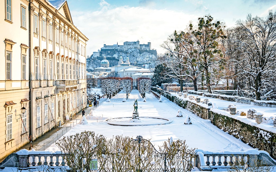 Mirabell Gardens in Salzburg covered in winter snow with Hohensalzburg Fortress in the background.