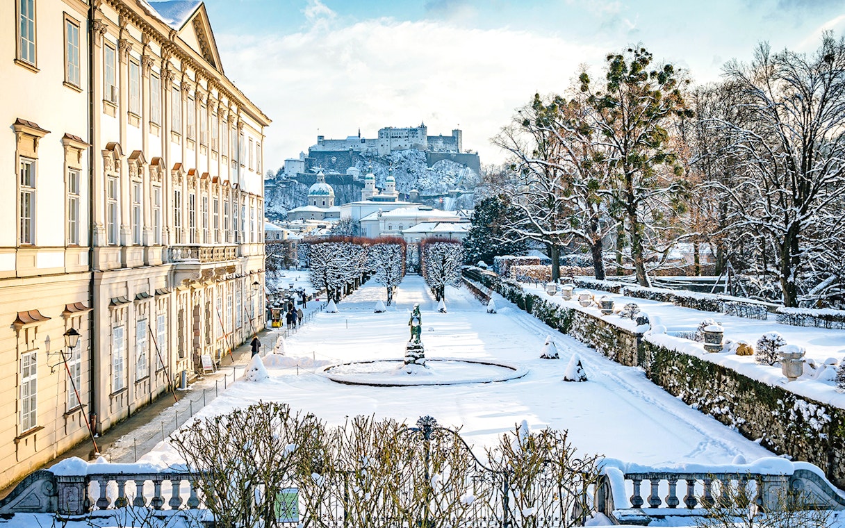 Mirabell Gardens in Salzburg covered in winter snow with Hohensalzburg Fortress in the background.