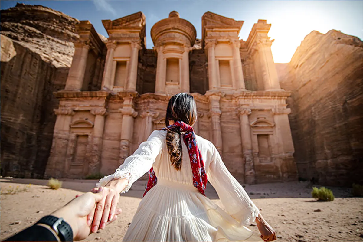 Tourist holding hands in front of Petra's Monastery, Jordan, during a guided day trip from Amman.