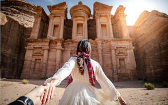 Tourist holding hands in front of Petra's Monastery, Jordan, during a guided day trip from Amman.