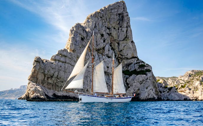 Sailing ship near rocky cliffs on Calanques Exploration Cruise.