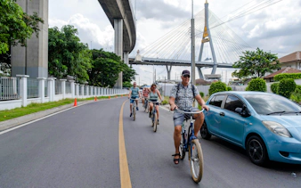 Cyclists riding under Bangkok's Bhumibol Bridge during a city tour.