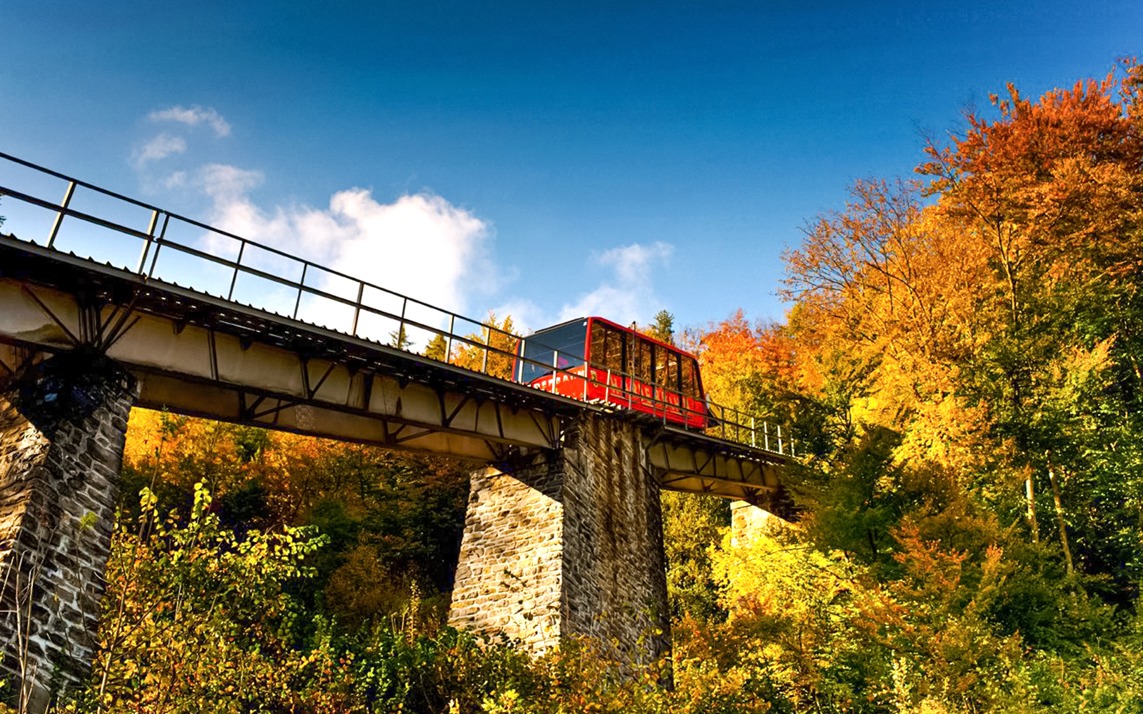 Red funicular on Harder Kulm bridge surrounded by autumn trees in Switzerland.