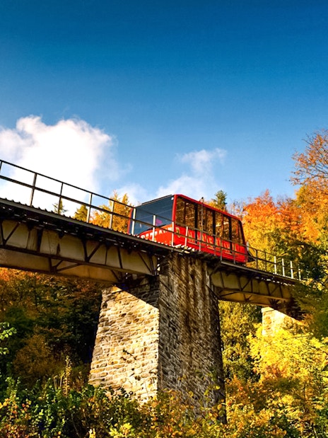 Red funicular on Harder Kulm bridge surrounded by autumn trees in Switzerland.