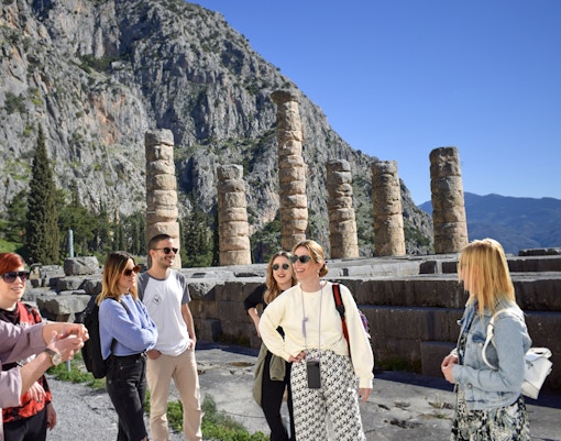 Visitors exploring ancient ruins at Delphi, Greece, with mountainous backdrop.