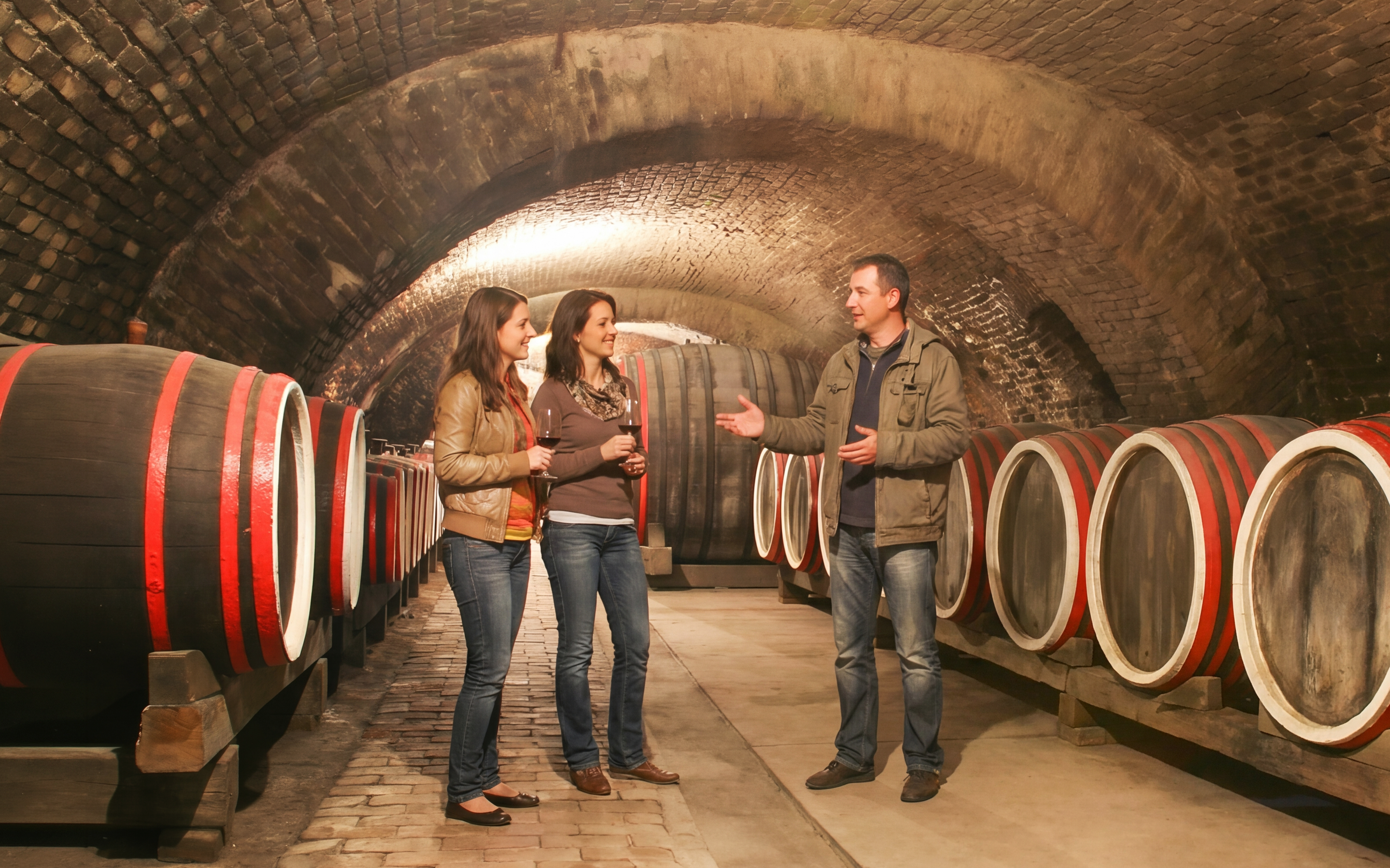 Tour group in an old wine cellar with large wooden barrels.