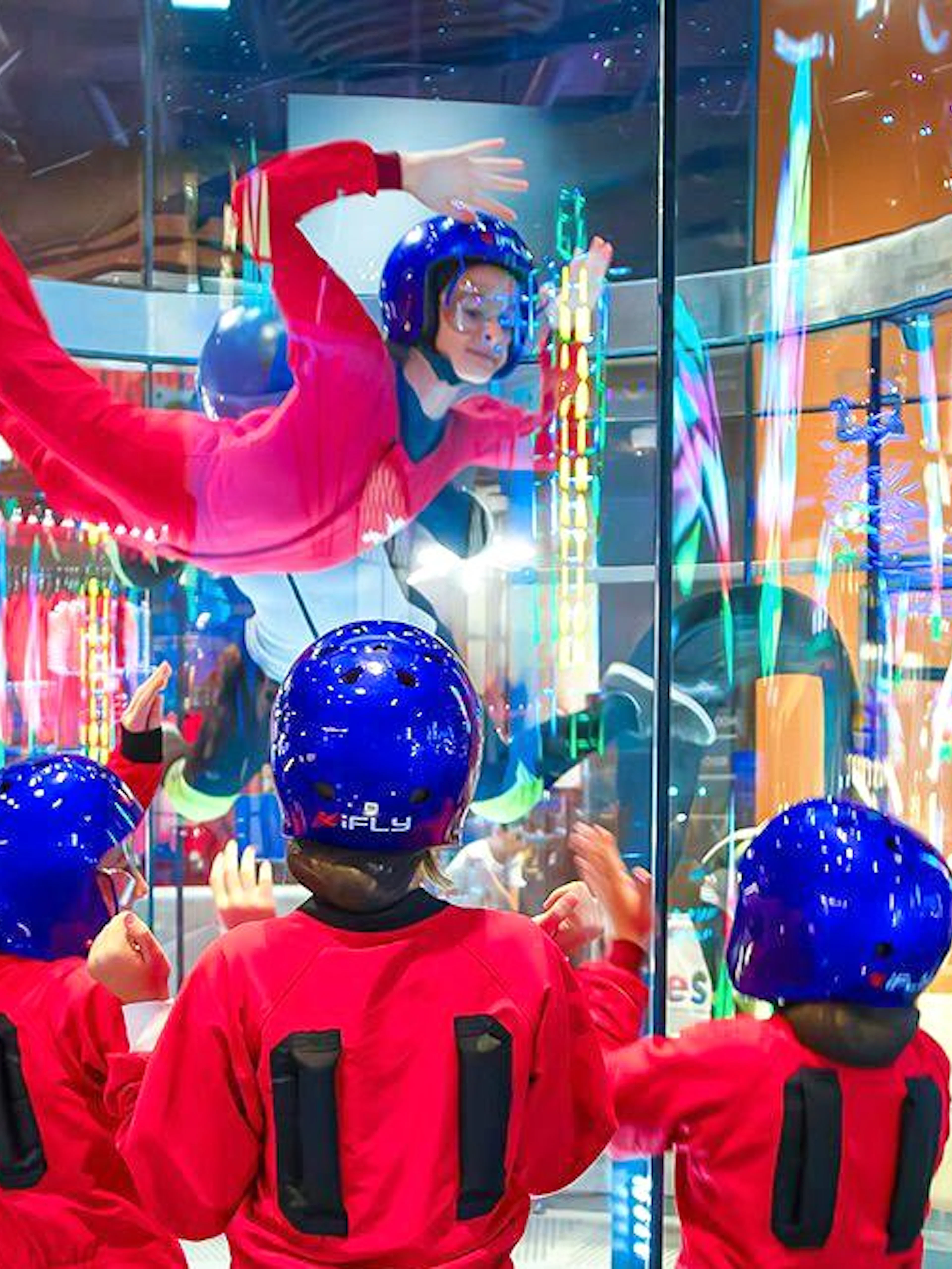 Indoor skydiving experience at iFLY with children watching in flight suits and helmets.