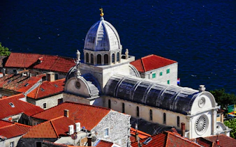Šibenik Cathedral with red-tiled roofs and Adriatic Sea in the background, Croatia.