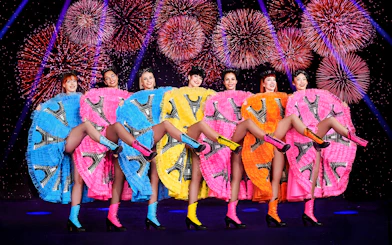 Dancers in colorful dresses performing at Pardis Latin, Paris with fireworks in the background.