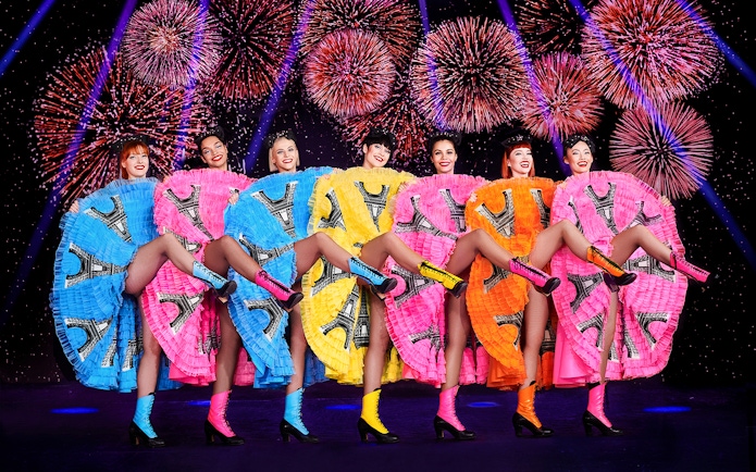 Dancers in colorful dresses performing at Pardis Latin, Paris with fireworks in the background.