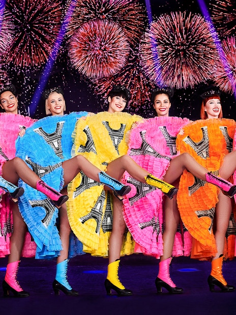 Dancers in colorful dresses performing at Pardis Latin, Paris with fireworks in the background.