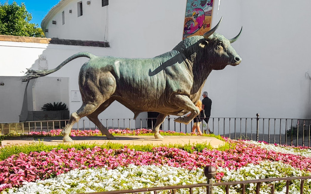 Monumento al Toro statue surrounded by flowers in Ronda, Spain.