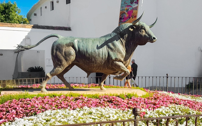 Monumento al Toro statue surrounded by flowers in Ronda, Spain.