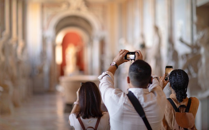 Tourists photographing sculptures in Vatican Museums hallway.