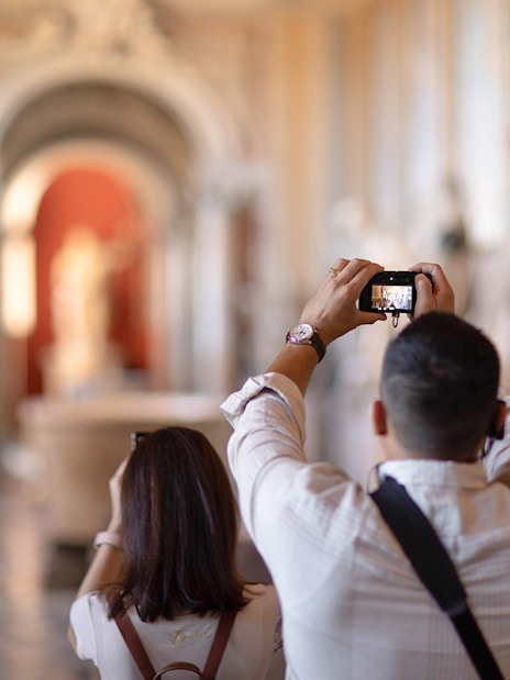 Tourists photographing sculptures in Vatican Museums hallway.