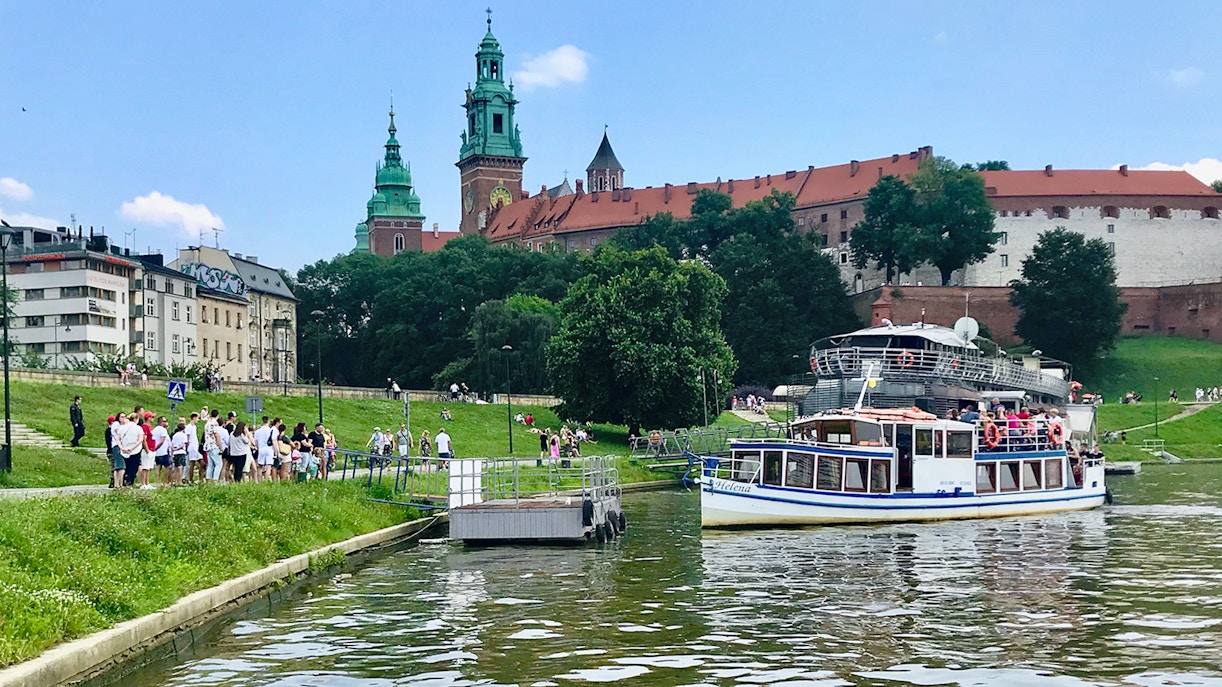Sightseeing boat on Vistula River near Wawel Castle, Krakow, with tourists boarding.