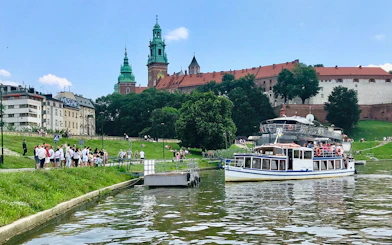 Sightseeing boat on Vistula River near Wawel Castle, Krakow, with tourists boarding.