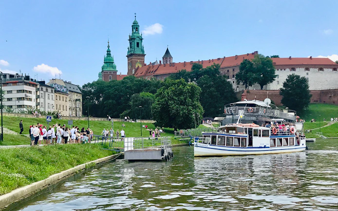 Sightseeing boat on Vistula River near Wawel Castle, Krakow, with tourists boarding.
