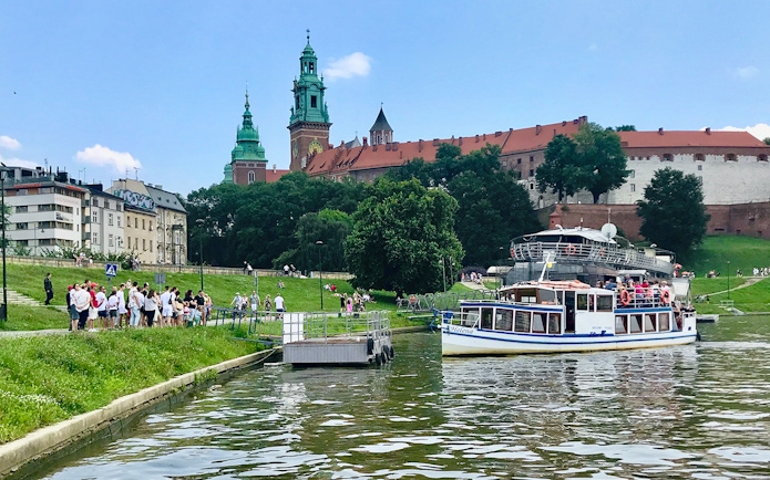 Sightseeing boat on Vistula River near Wawel Castle, Krakow, with tourists boarding.