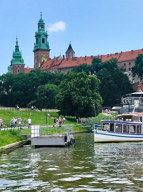 Sightseeing boat on Vistula River near Wawel Castle, Krakow, with tourists boarding.