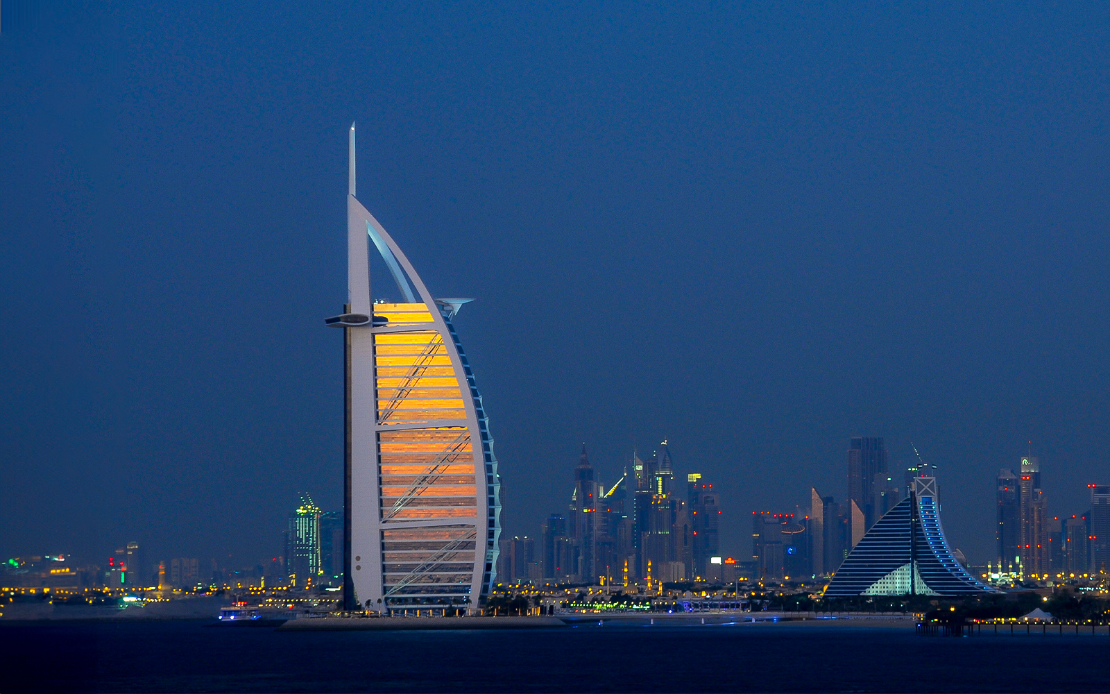 Burj Al Arab illuminated at night with Dubai skyline in the background.