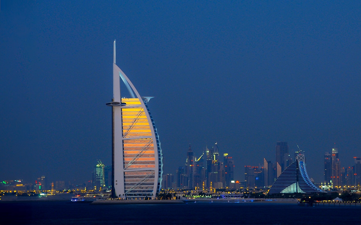 Burj Al Arab illuminated at night with Dubai skyline in the background.