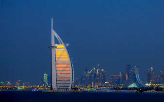 Burj Al Arab illuminated at night with Dubai skyline in the background.