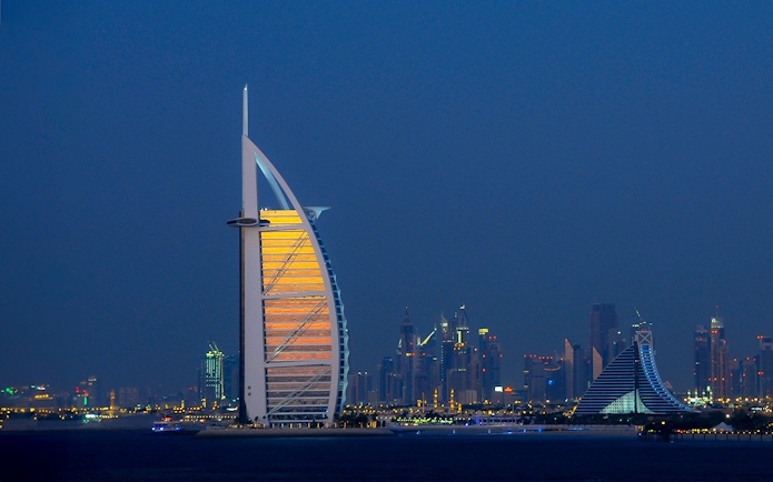 Burj Al Arab illuminated at night with Dubai skyline in the background.