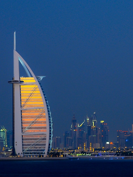 Burj Al Arab illuminated at night with Dubai skyline in the background.