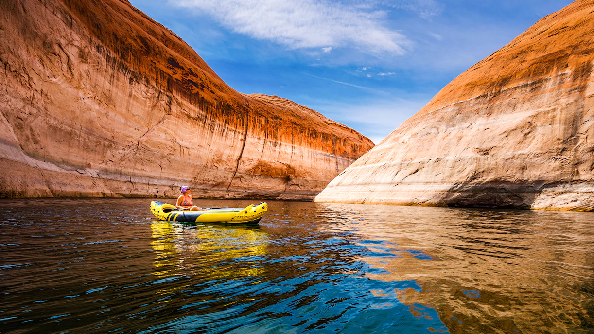 Kayaker paddling through narrow canyon walls on Lake Powell, Arizona.