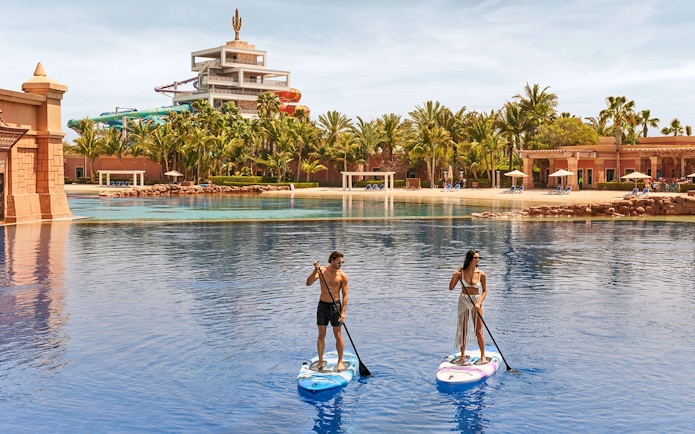 Tourists paddleboarding at Atlantis, The Palm, Dubai with water slides in the background.