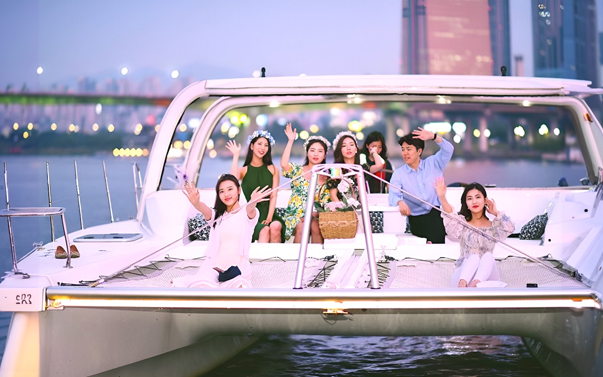 Group enjoying a yacht ride on the Han River, Seoul, with city lights in the background.
