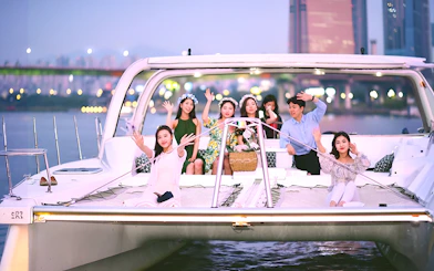Group enjoying a yacht ride on the Han River, Seoul, with city lights in the background.