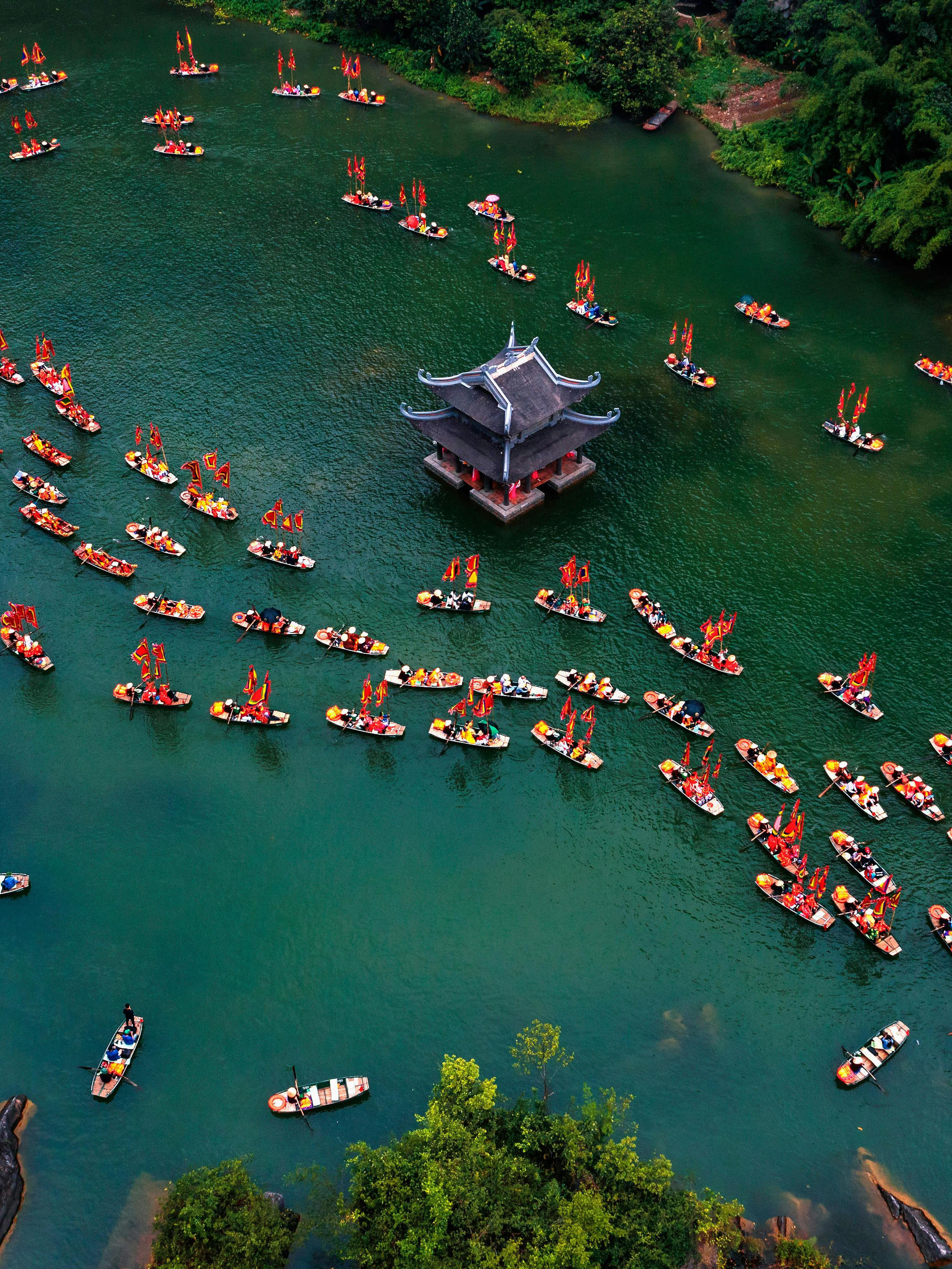 Boats with red flags on a river near a pagoda in Trang An, Ninh Binh, Vietnam.