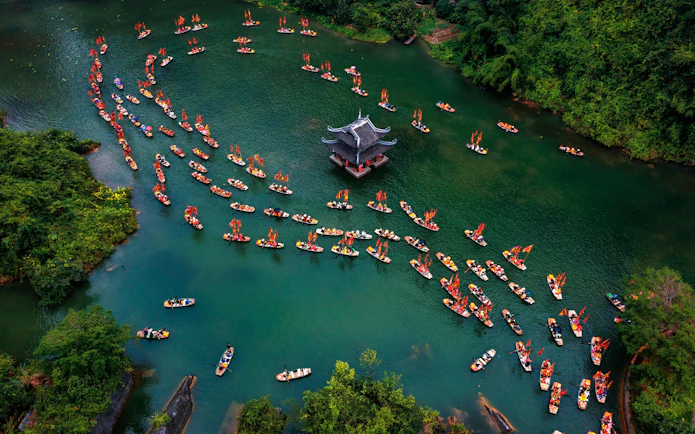 Boats with red flags on a river near a pagoda in Trang An, Ninh Binh, Vietnam.