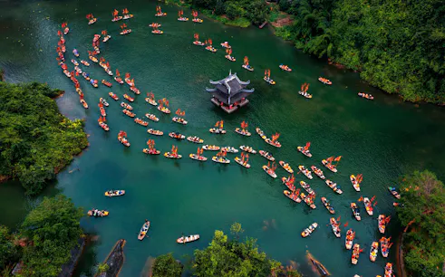 Boats with red flags on a river near a pagoda in Trang An, Ninh Binh, Vietnam.