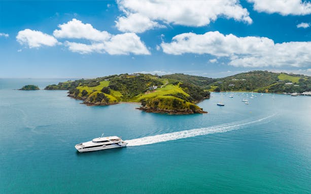 Ferry approaching Waiheke Island, New Zealand, with lush green hills and sailboats in the bay.