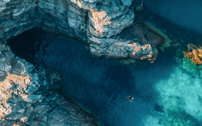 Swimmer near rocky cliffs and clear waters of Blue Cave, Dubrovnik.