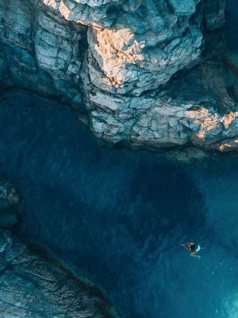 Swimmer near rocky cliffs and clear waters of Blue Cave, Dubrovnik.