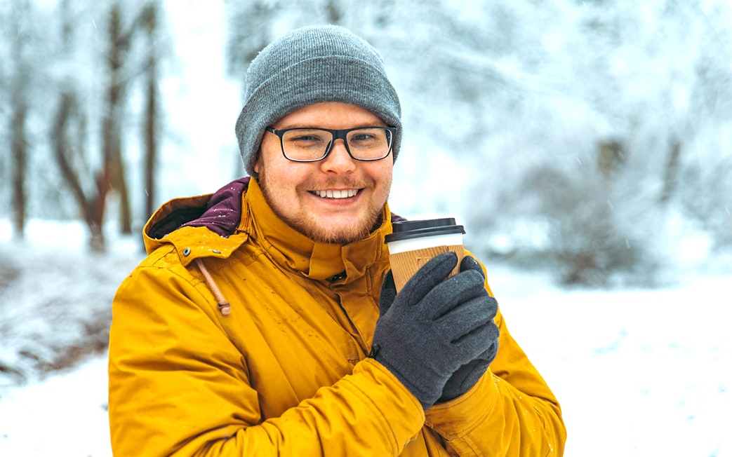 Guest holding a warm drink in a snowy Sami tent after reindeer sledding in Tromso, Norway.