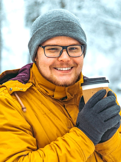 Guest holding a warm drink in a snowy Sami tent after reindeer sledding in Tromso, Norway.