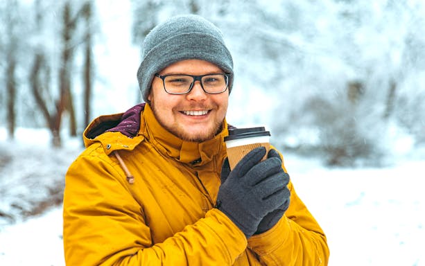 Guest holding a warm drink in a snowy Sami tent after reindeer sledding in Tromso, Norway.