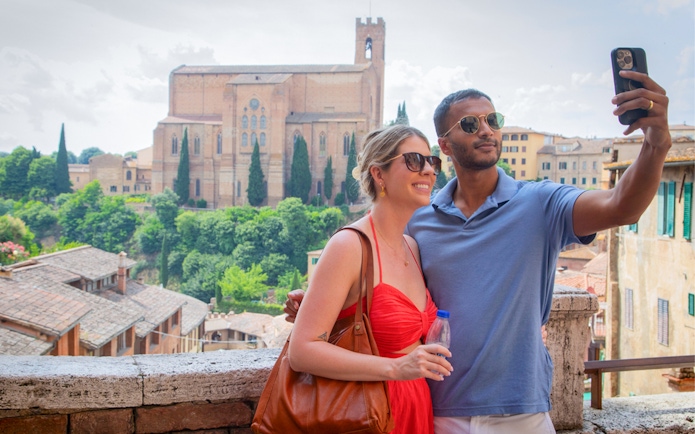 Couple taking a selfie with Basilica of San Domenico in Siena, Tuscany in the background.