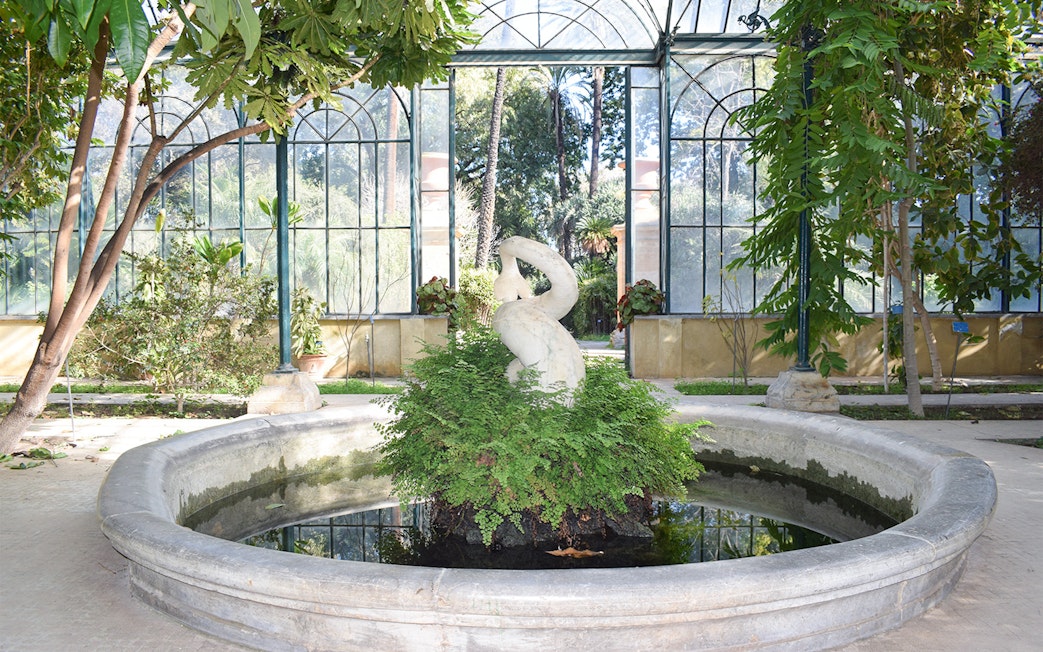 Sculpture in greenhouse at Orto Botanico, Palermo, surrounded by lush greenery.
