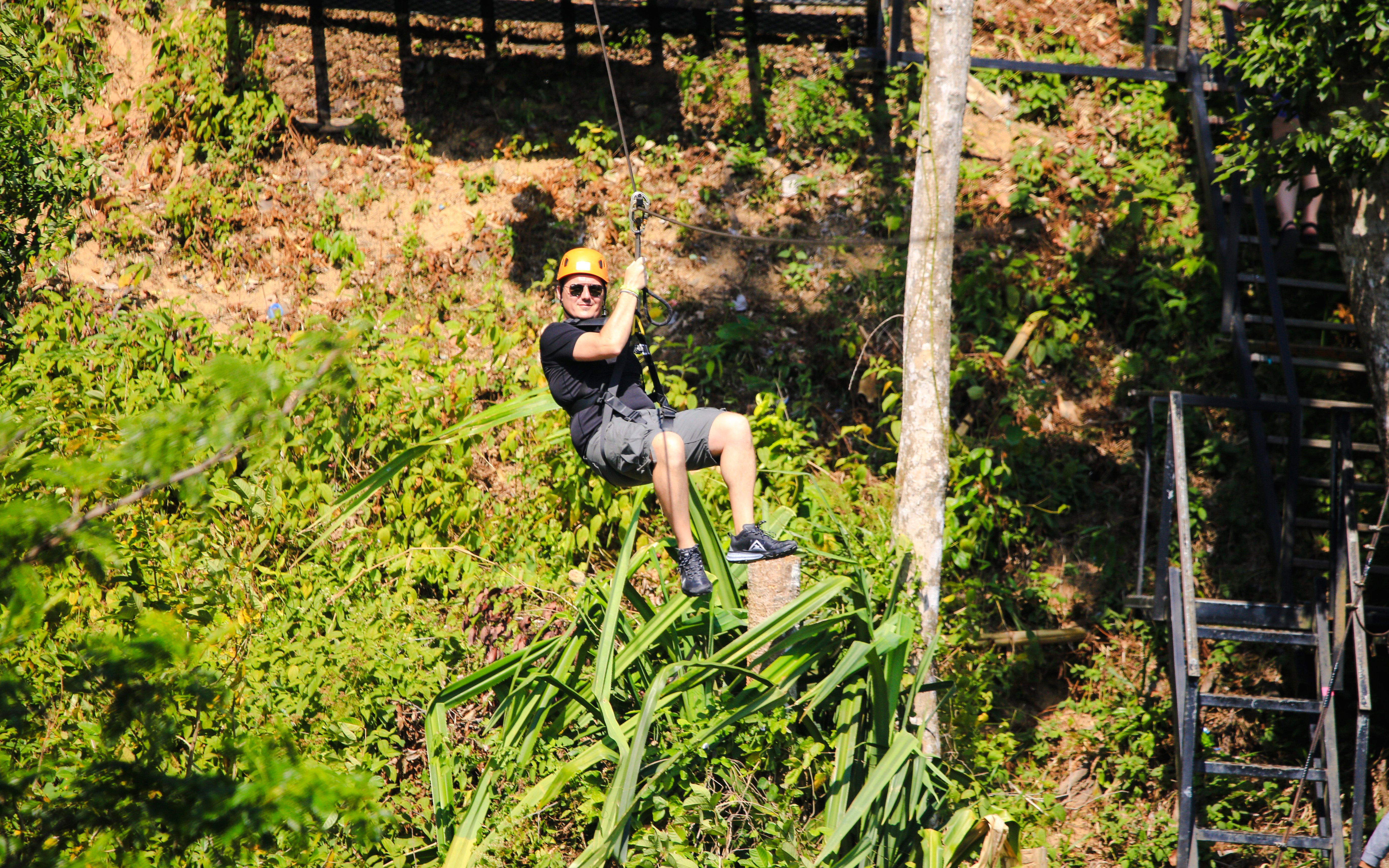 Guy ziplining through lush forest landscape.